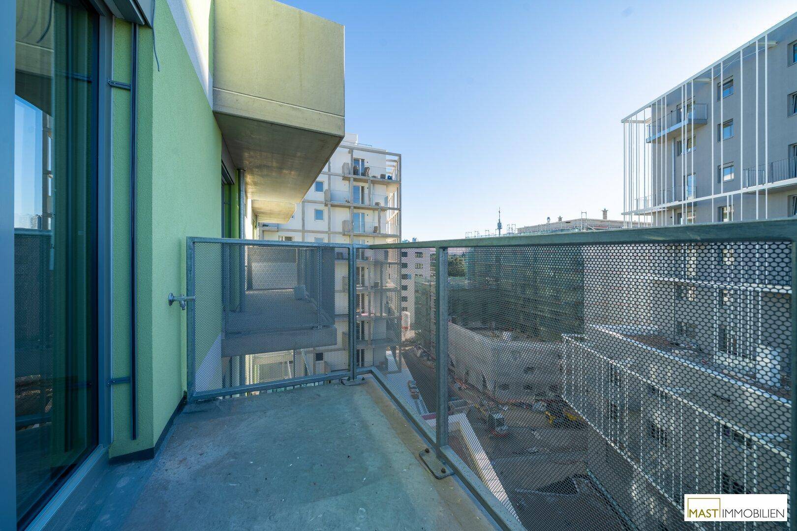 Geräumiger Balkon mit perforiertem Metallgeländer und Blick auf die umliegenden Neubauten.