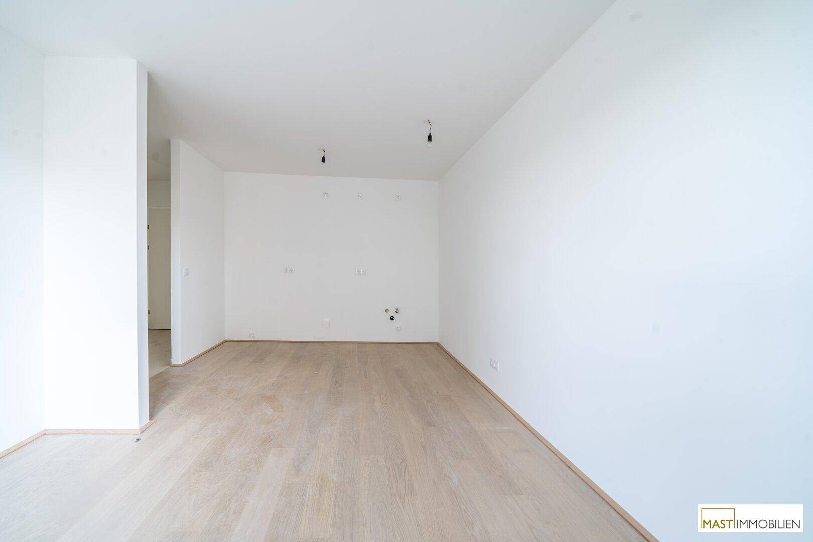 Leerer, heller Raum mit Parkettboden und einem Durchgang zu einem angrenzenden Bereich.