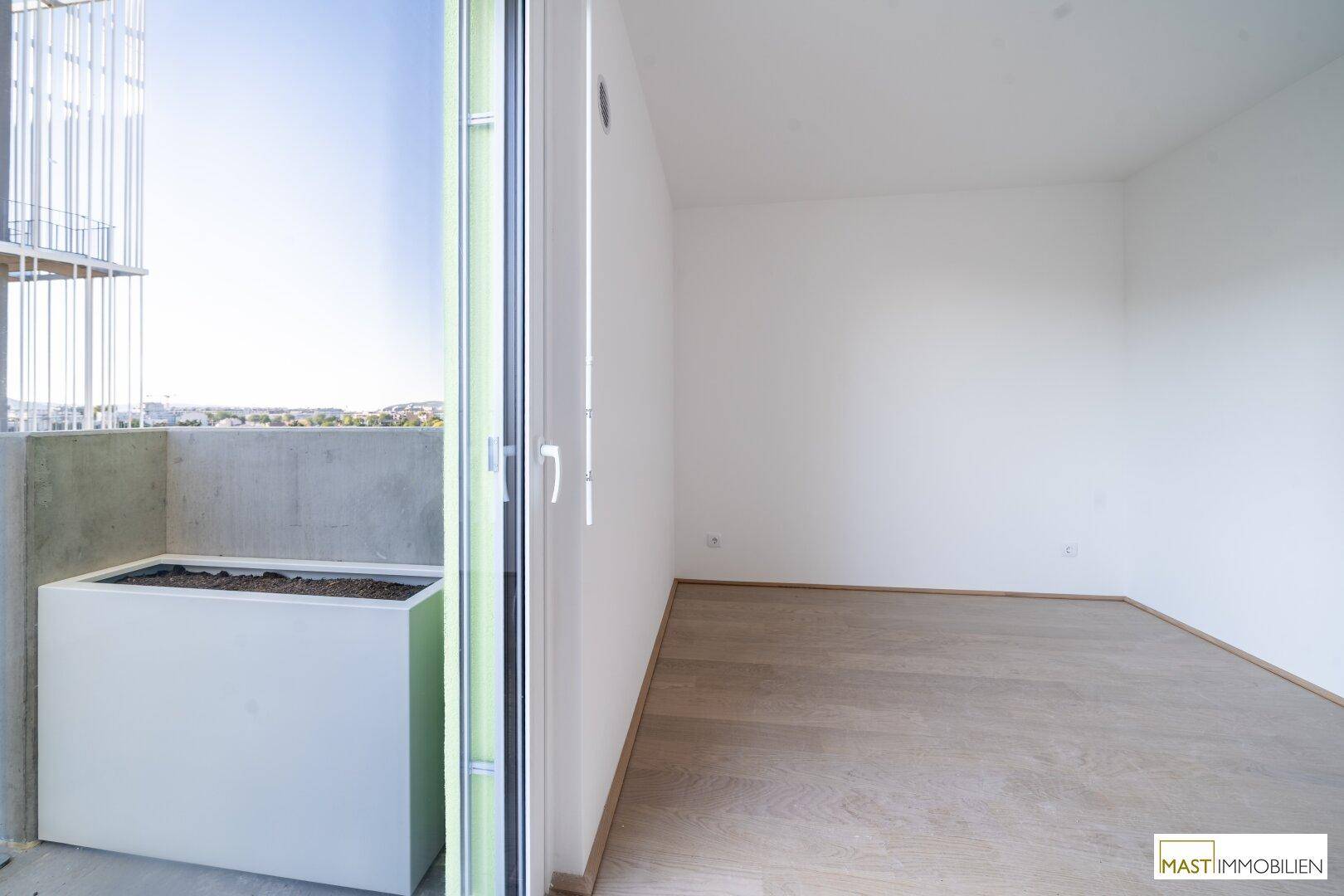 Heller Innenraum mit Blick auf den Balkon und die grüne Umgebung durch die große Glastür.