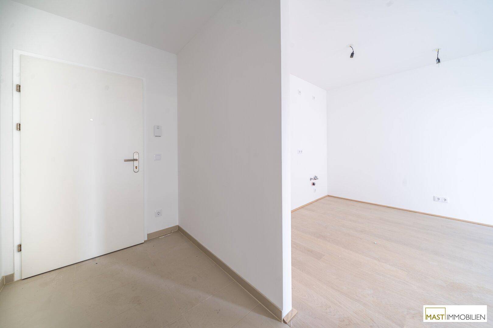 Eingangsbereich mit heller Tür und Übergang zu einem weiteren, unmöblierten Zimmer.