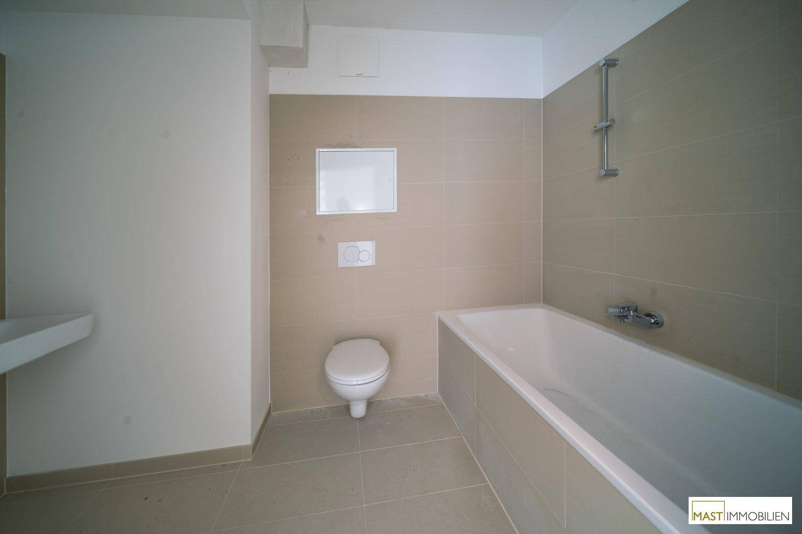 Modernes Badezimmer mit Badewanne und Wand-WC in hellen, neutralen Fliesen.