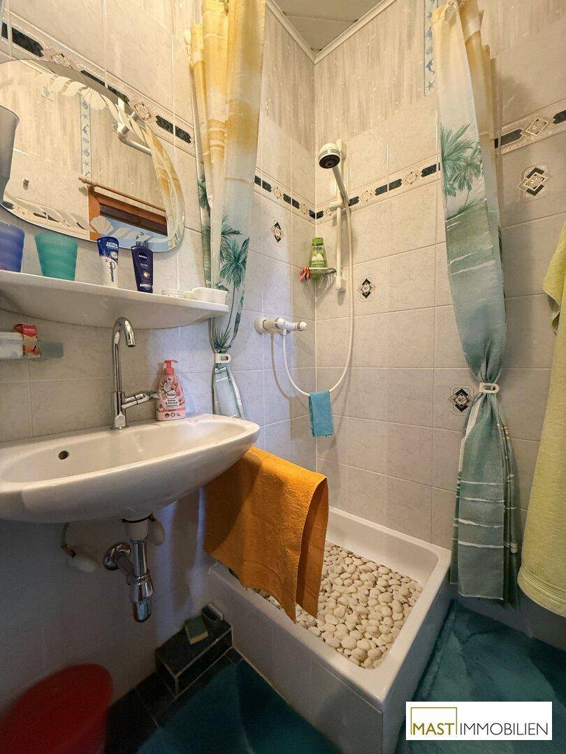 Badezimmer mit Waschbecken, Spiegel und einer Dusche mit Kieselsteinboden.