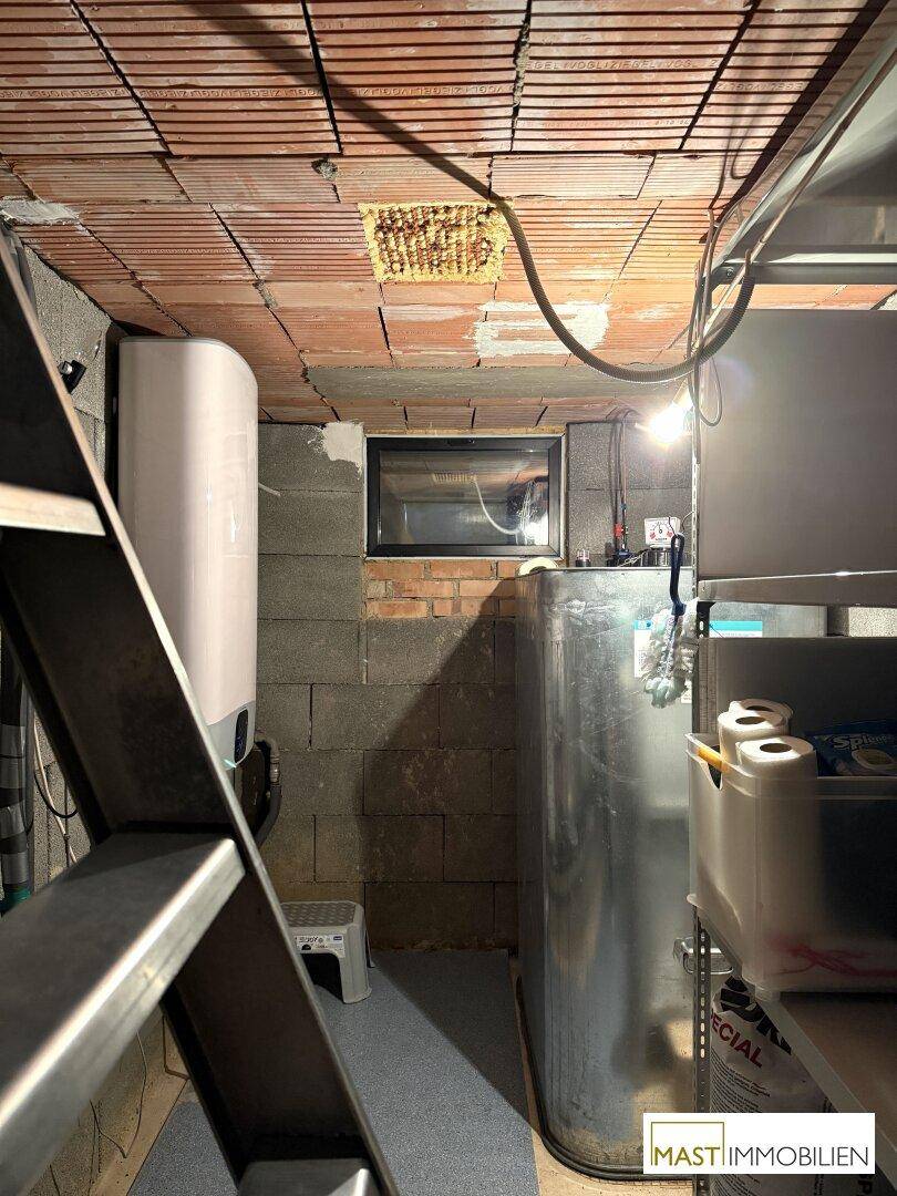 Kellerraum mit unverputzten Wänden, Warmwasserbereiter und großem Wassertank.