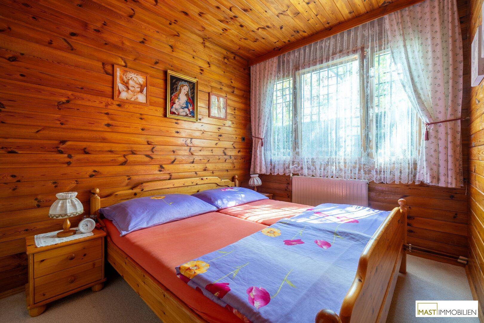 Schlafzimmer mit Holztäfelung, zwei Einzelbetten und einem großen Fenster mit Vorhängen.