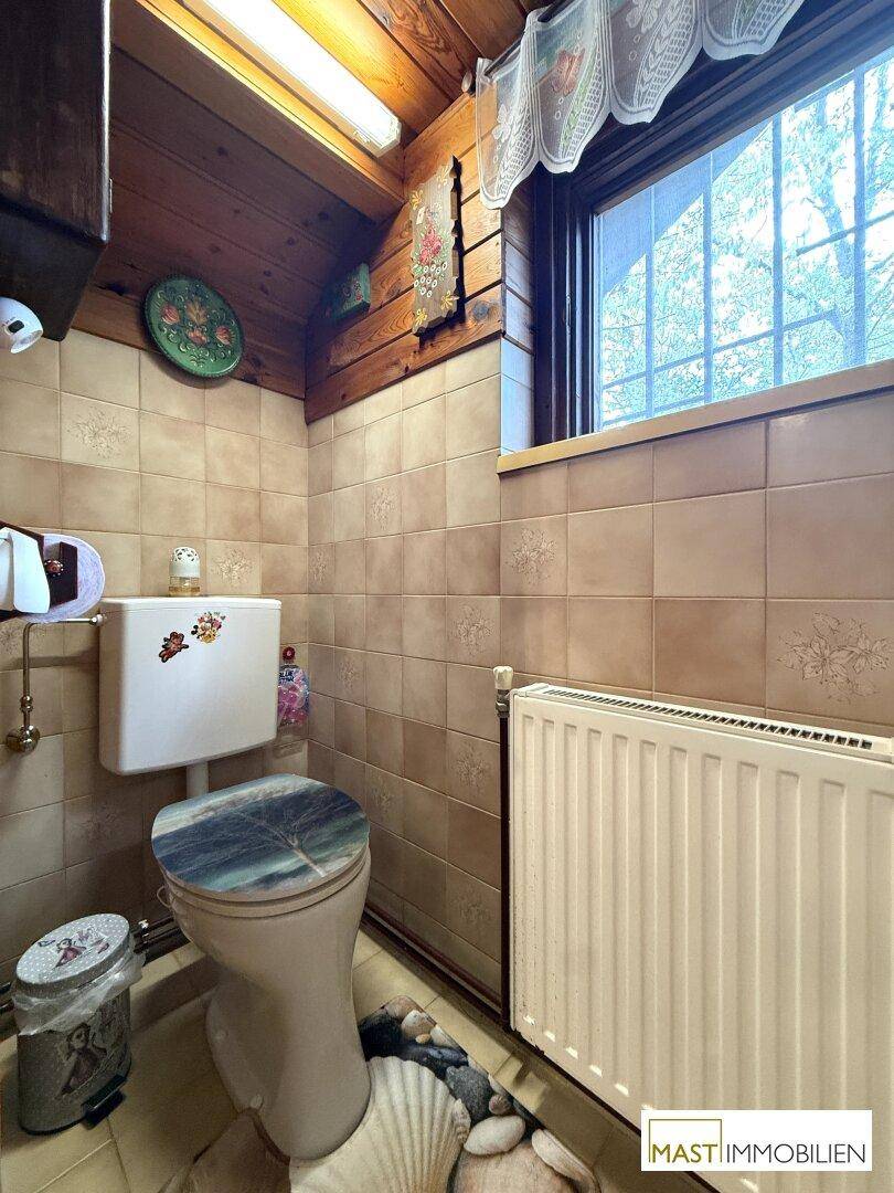 Separate Toilette mit Fenster, Heizkörper und Fliesen an den Wänden.