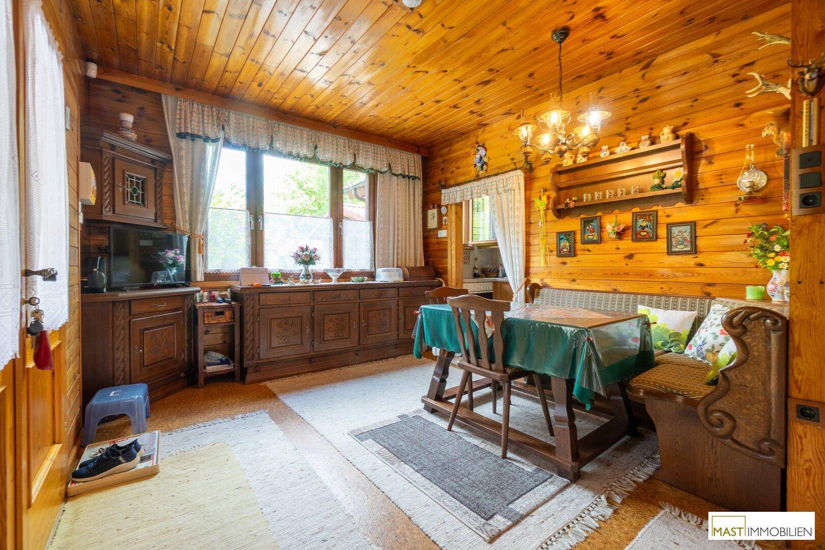 Rustikaler Wohn-Essbereich mit Holzwänden, traditionellen Möbeln und einem großen Fenster.