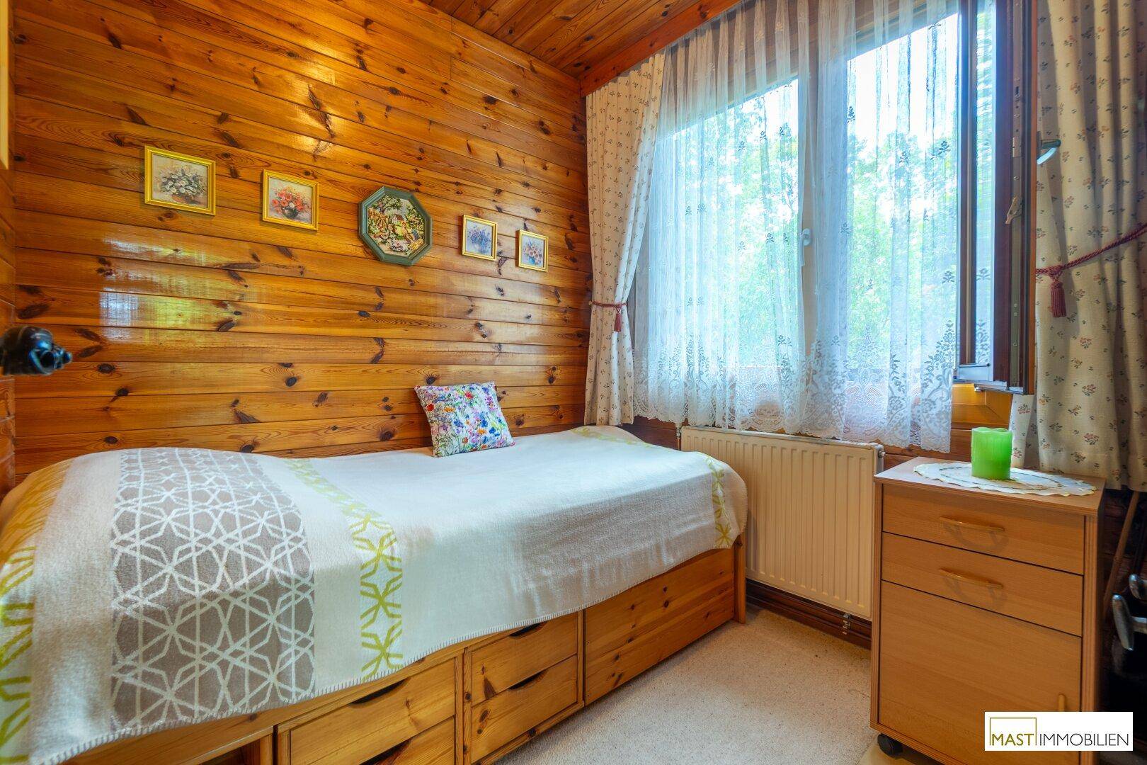 Einzelzimmer mit Holztäfelung, Bett mit Stauraum und einem Fenster für natürliches Licht.