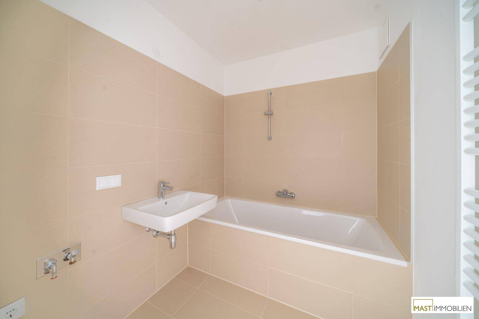 Modernes Badezimmer mit beigefarbenen Fliesen, Badewanne und Waschbecken.