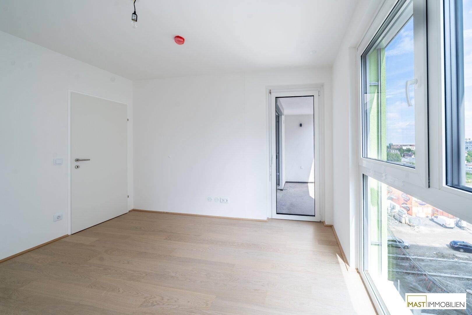 Helles Schlafzimmer mit Parkettboden und weitem Blick über die Stadt.