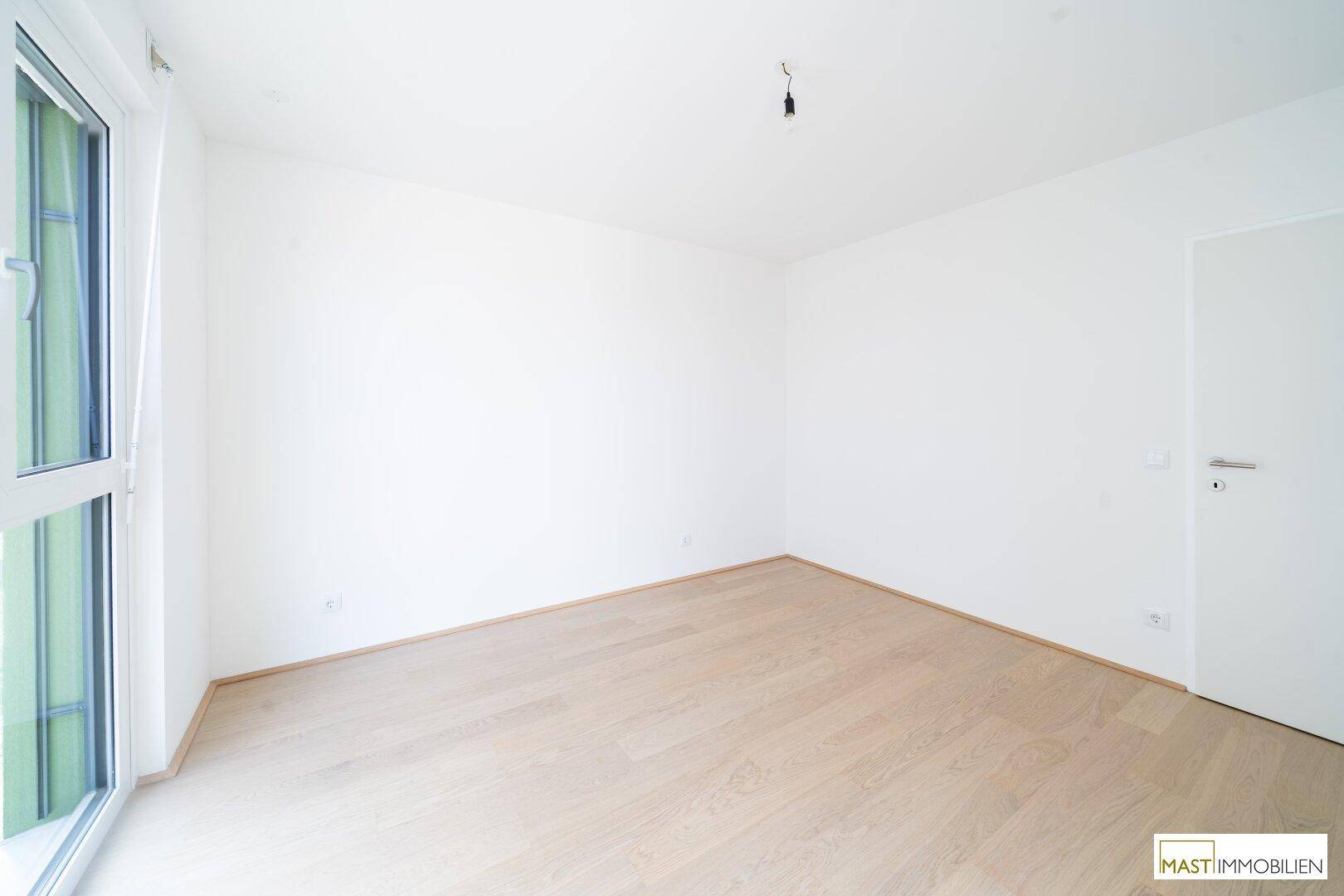 Leeres Schlafzimmer mit hellem Parkettboden und großen Fenstern.