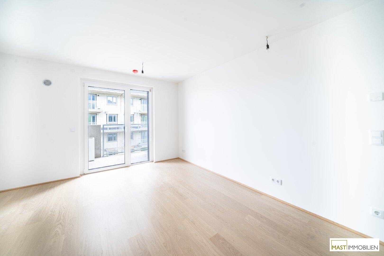 Helles Wohnzimmer mit Parkettboden und Zugang zu einem Außenbereich.