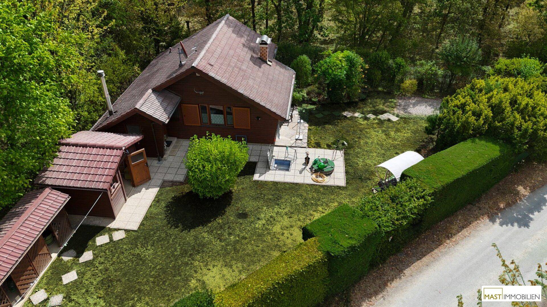 Blick von oben auf das Haus mit weitläufigem Garten, Rasenfläche und kleiner Terrasse.