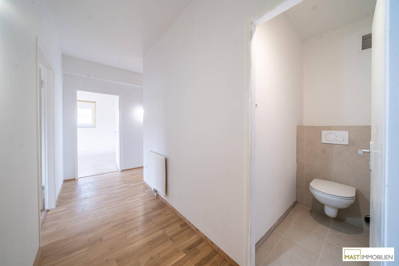 Separates Gäste-WC mit wandhängender Toilette und hellen Fliesen an Wänden und Boden.