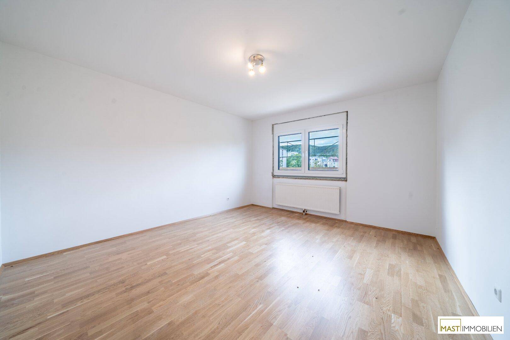 Geräumiges Schlafzimmer mit hellem Parkettboden und einem Fenster, das viel Tageslicht hereinlässt.