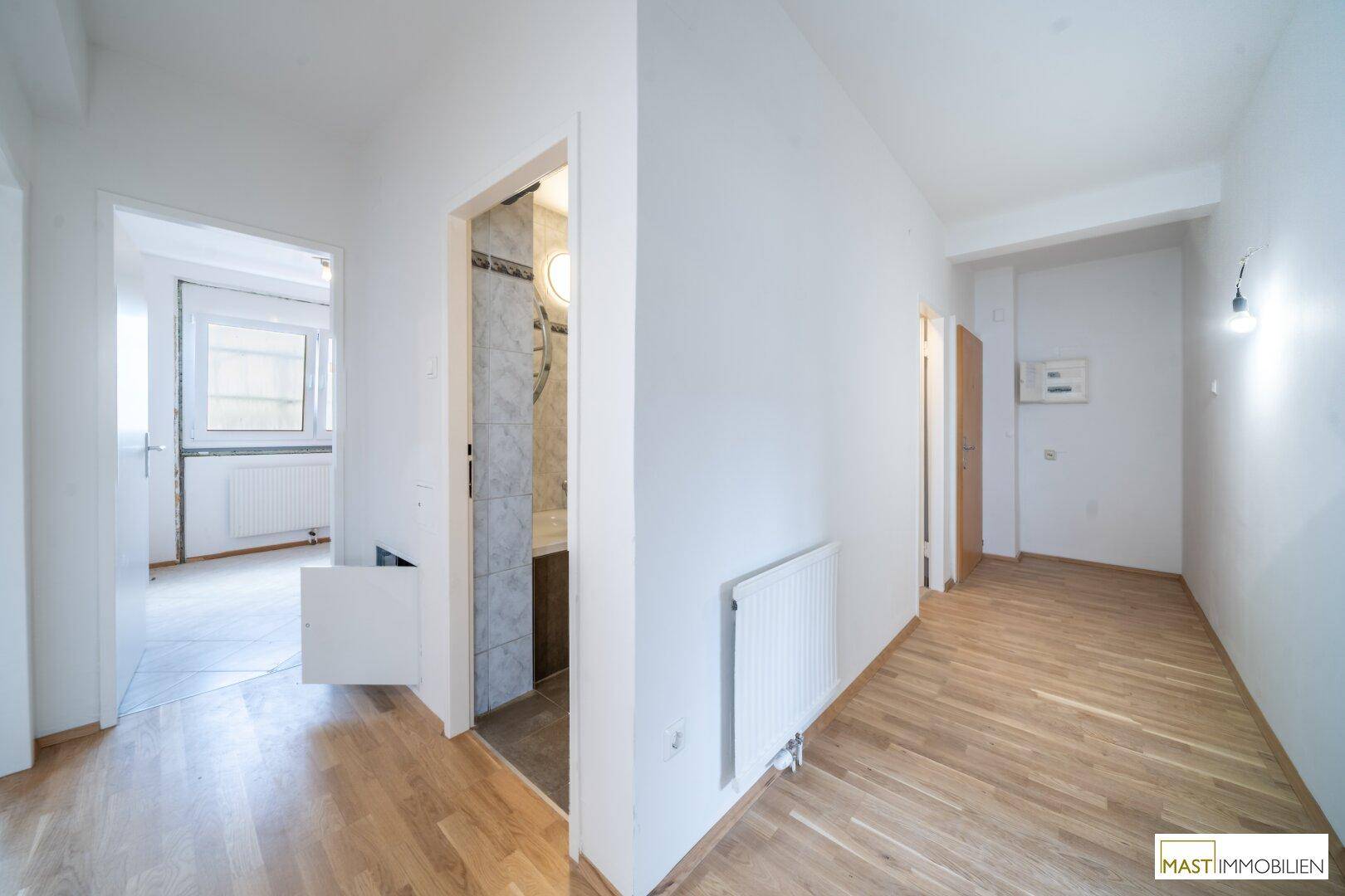 Heller Flur mit Parkettboden, weißen Wänden und Zugang zu verschiedenen Räumen der Wohnung.