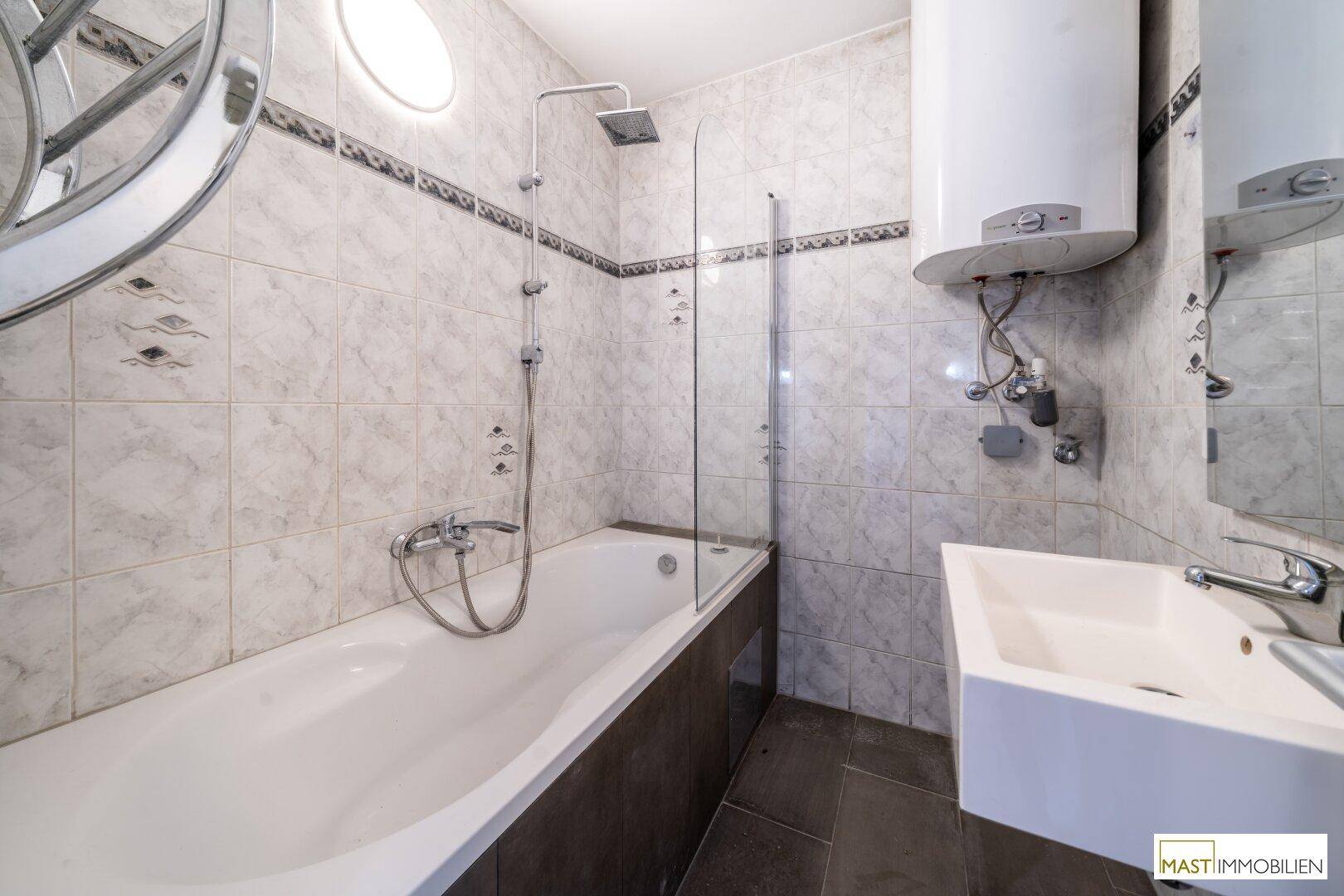 Gefliestes Badezimmer mit Badewanne, Duschfunktion und einem einzelnen Waschbecken.