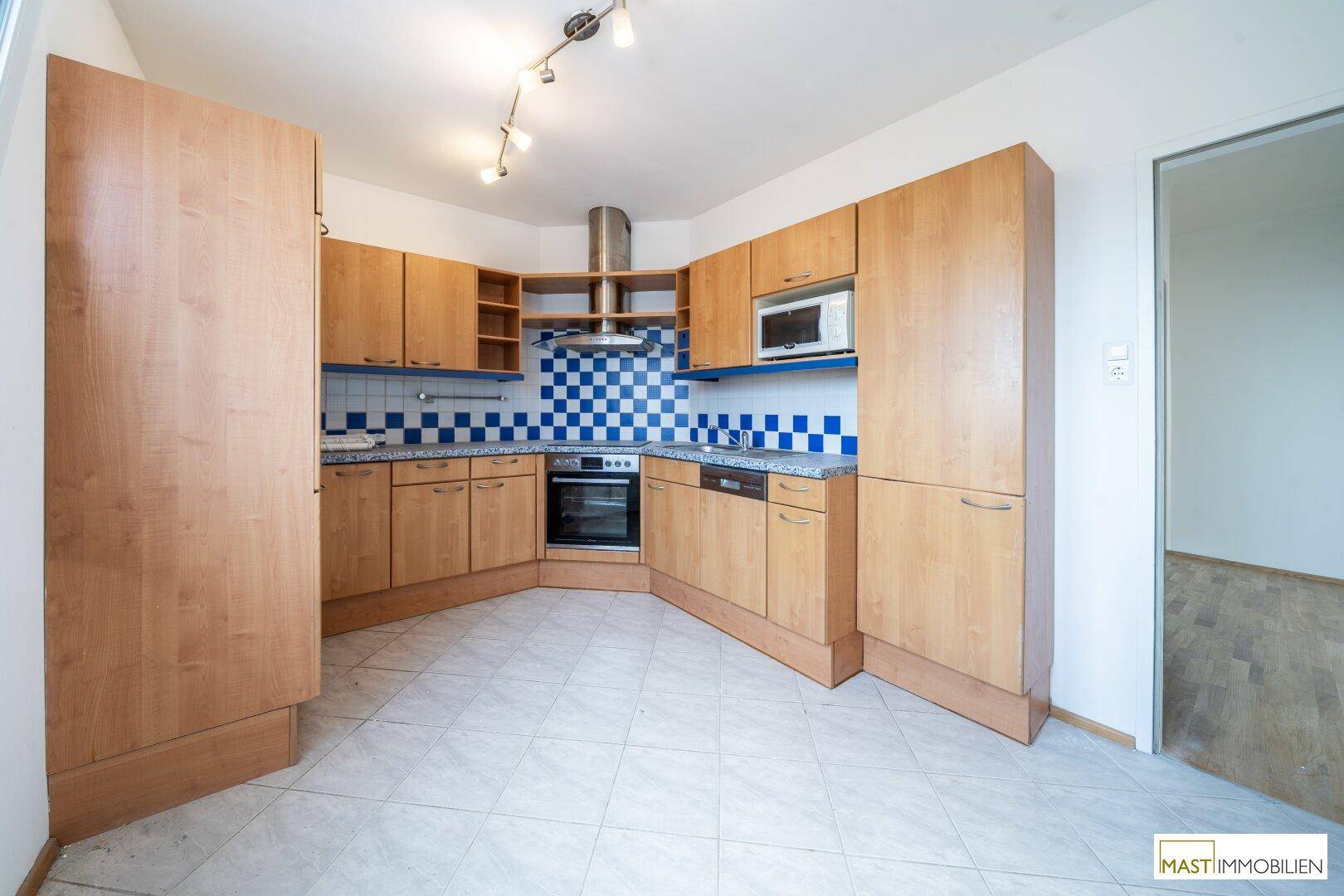 Funktionale Einbauküche mit Holzfronten, blauen Fliesen und integrierten Geräten.