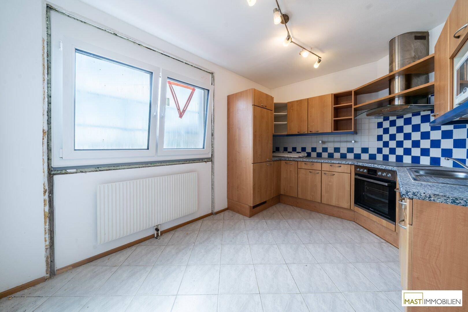Einbauküche mit Holzschränken, gefliestem Boden und einem Fenster, das Tageslicht spendet.