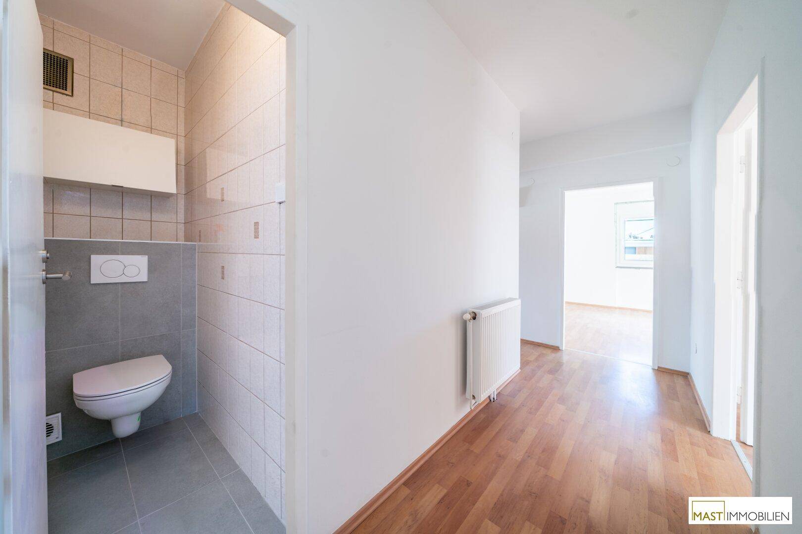 Separates WC mit wandhängender Toilette und modernen Fliesen in Grau und Weiß.