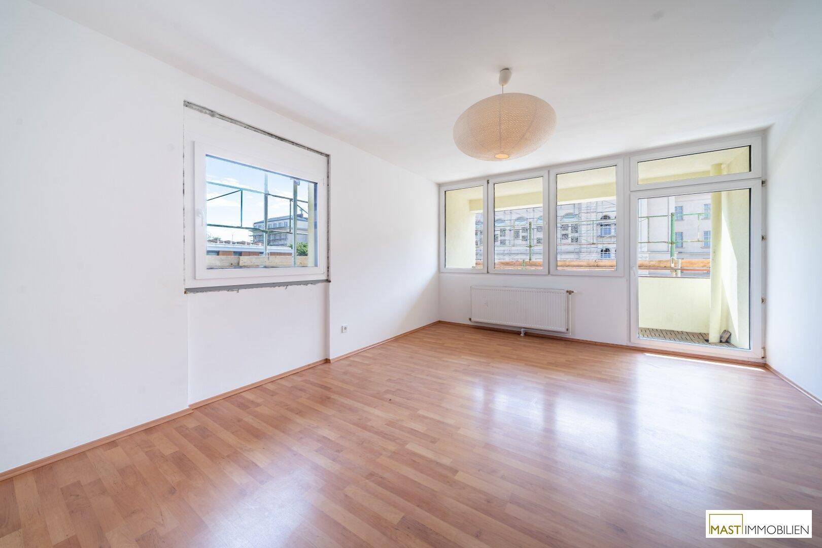 Heller Wohnraum mit Laminatboden, großen Fenstern und Zugang zum Balkon.