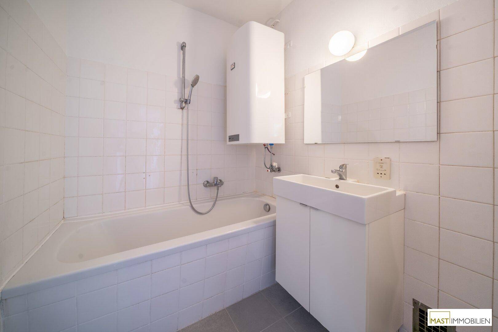Funktionales Badezimmer mit Badewanne, Waschbecken und weißen Wandfliesen.