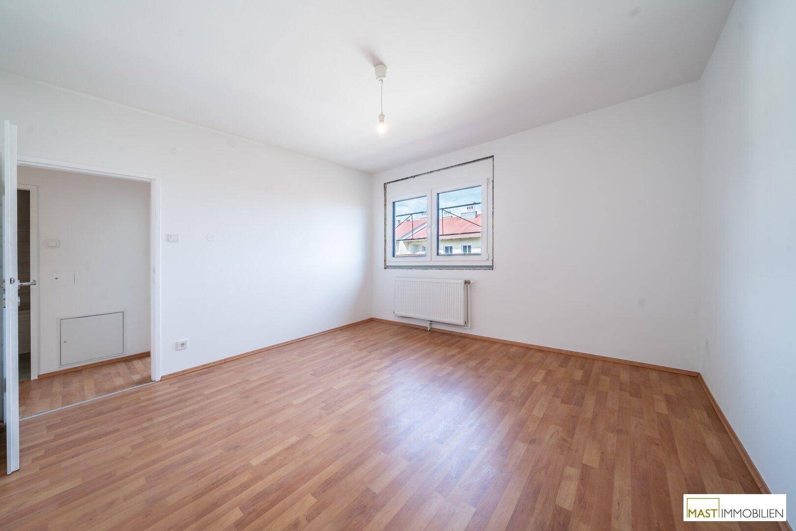 Freundliches Zimmer mit Laminatboden und Blick auf die Dächer der Umgebung.
