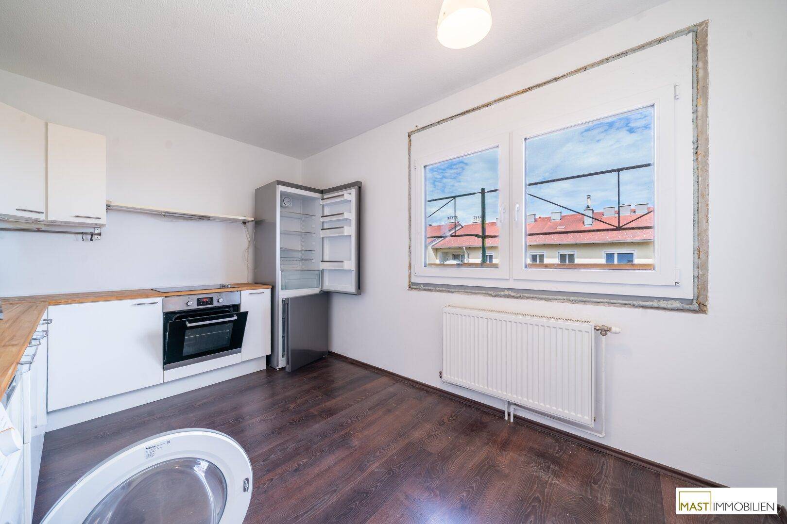 Helle Küche mit Fenster, weißen Schränken und dunklem Laminatboden.