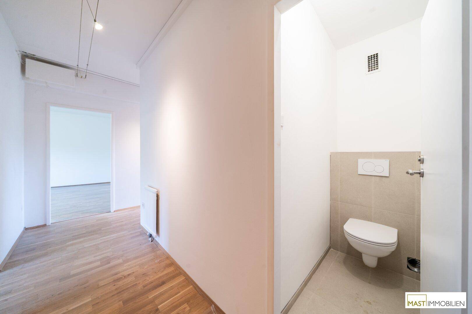 Separates WC mit wandhängender Toilette und hellen Fliesen im Eingangsbereich.
