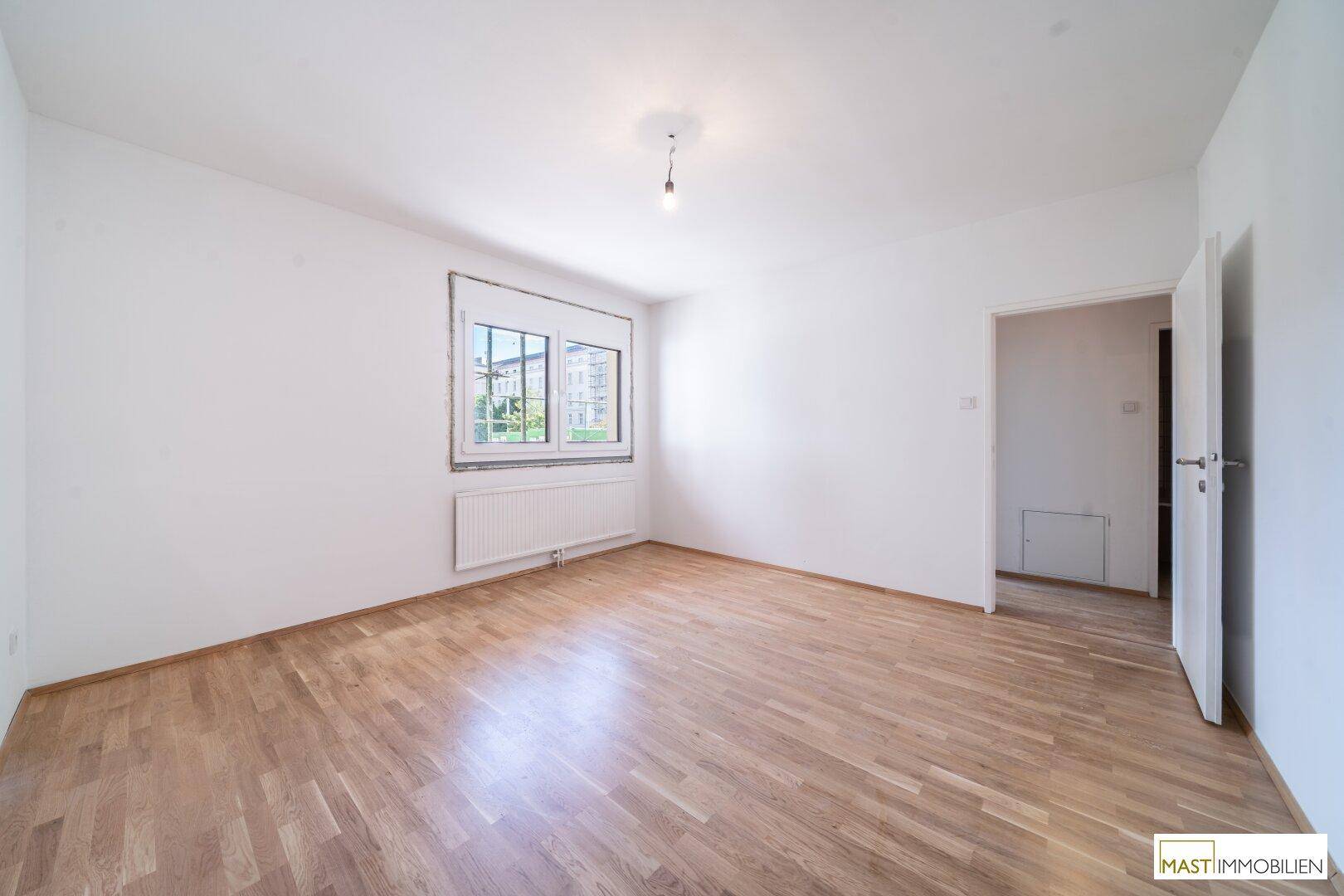 Geräumiges, leeres Zimmer mit Holzboden und Fenster, bereit zur individuellen Gestaltung.