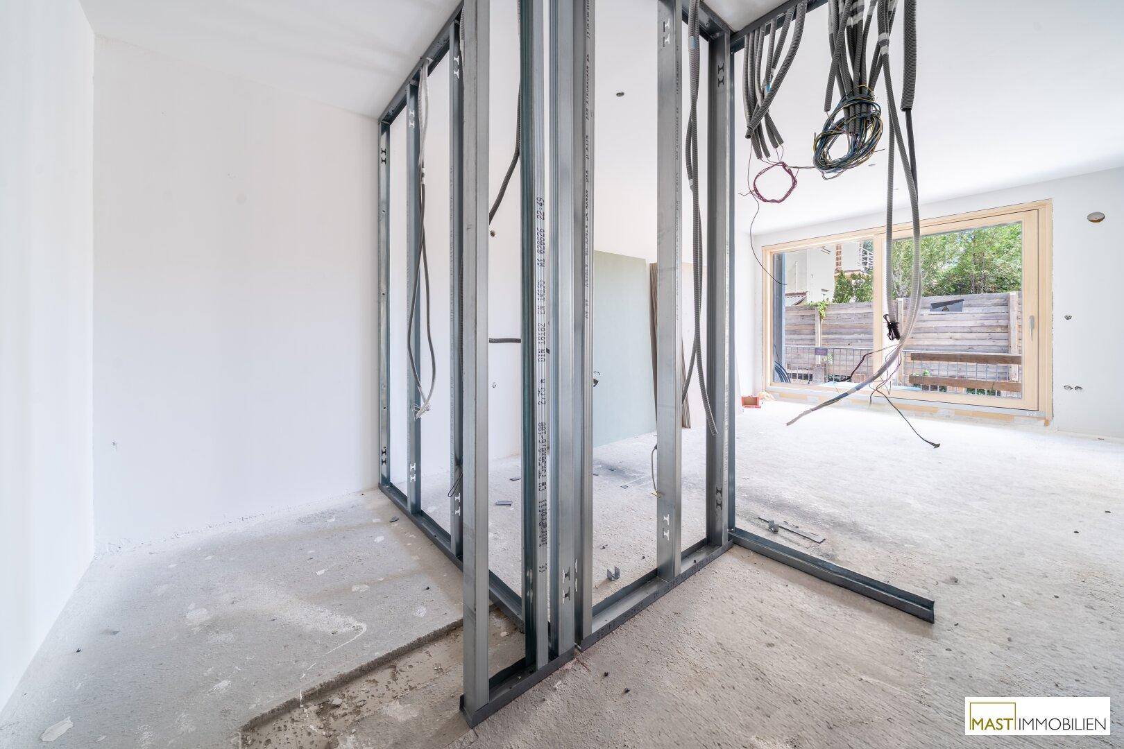 Rohbau-Innenraum mit großen Fensterfronten, Metallständerwerk und Blick ins Freie.