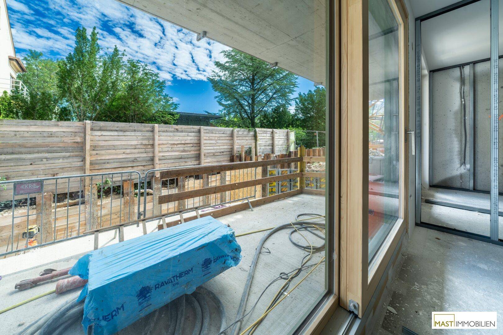 Blick aus dem Rohbau auf die Baustelle und die umgebende Holzumzäunung.