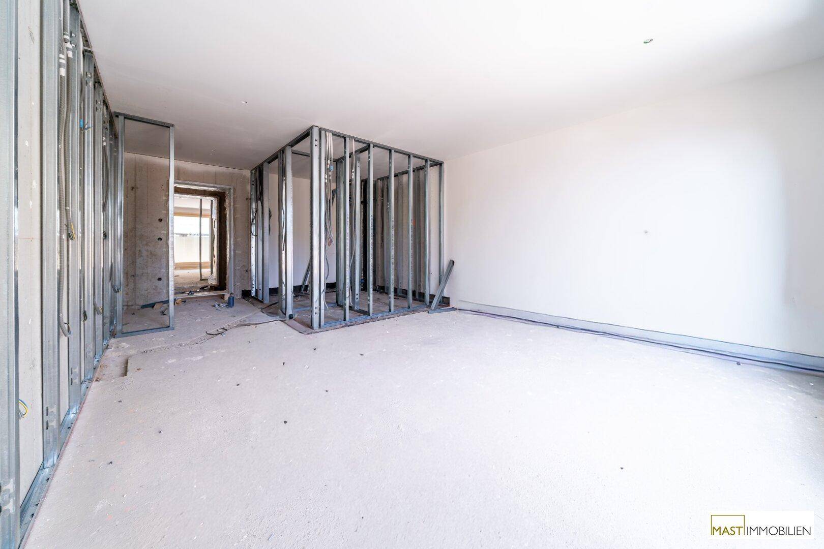Rohbau-Innenraum mit Metallständerwerk für zukünftige Wände und einem Betonboden, bereit für den weiteren Ausbau.