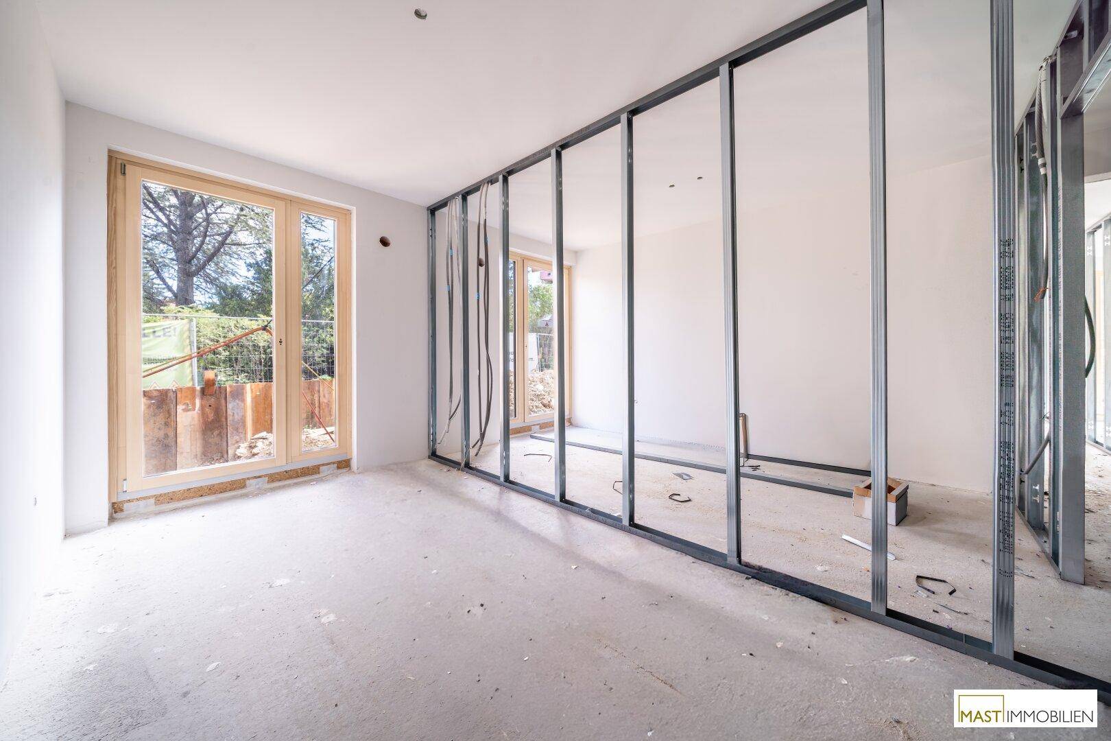 Rohbauzimmer mit Metallständerwerk für Wände und großen Fenstern, die viel Tageslicht hereinlassen.