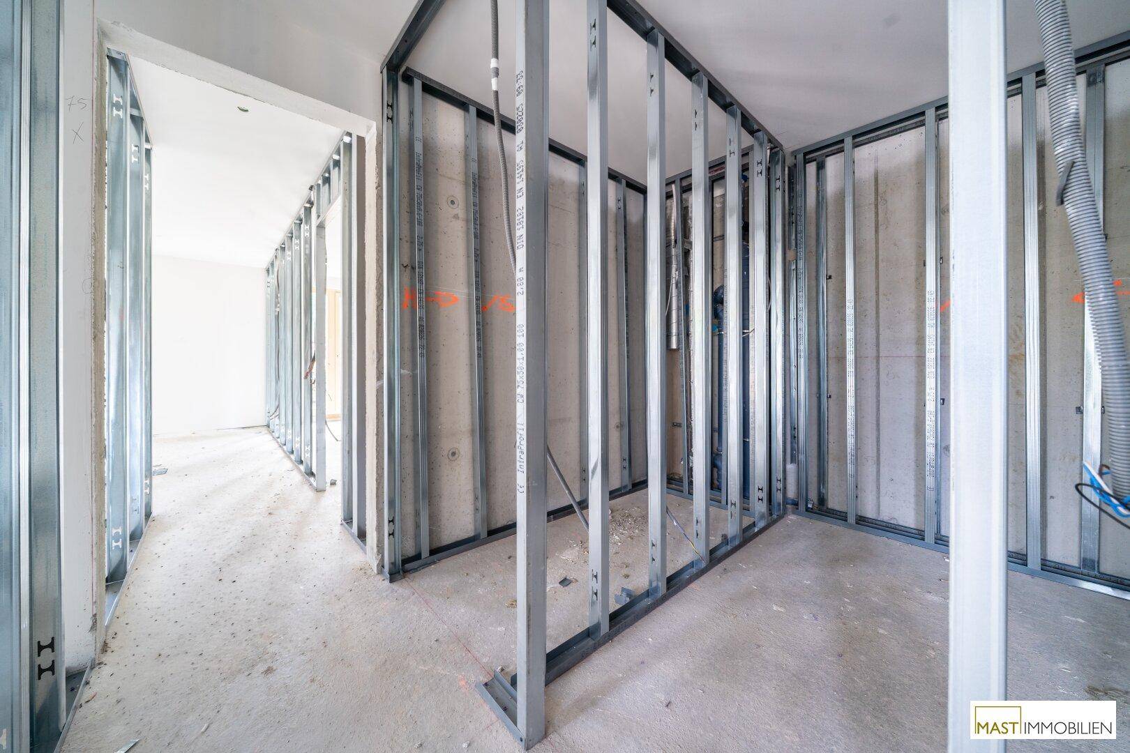 Unfertiger Flur mit Metallständerwerk für die Wände und Betonboden im Rohbauzustand.