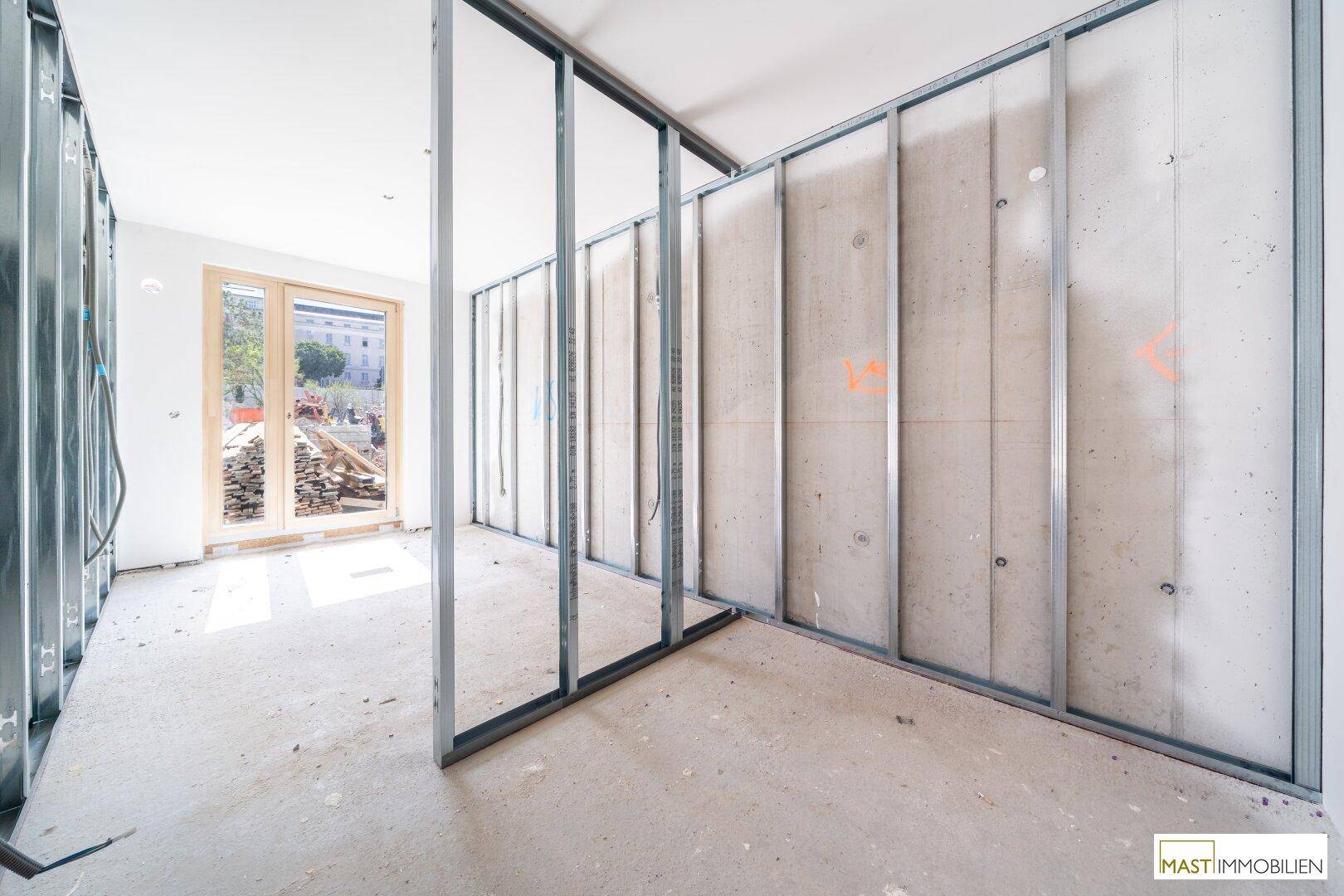 Innenraum im Rohbau mit sichtbaren Metallständerwänden und einer Tür, die nach draußen führt.