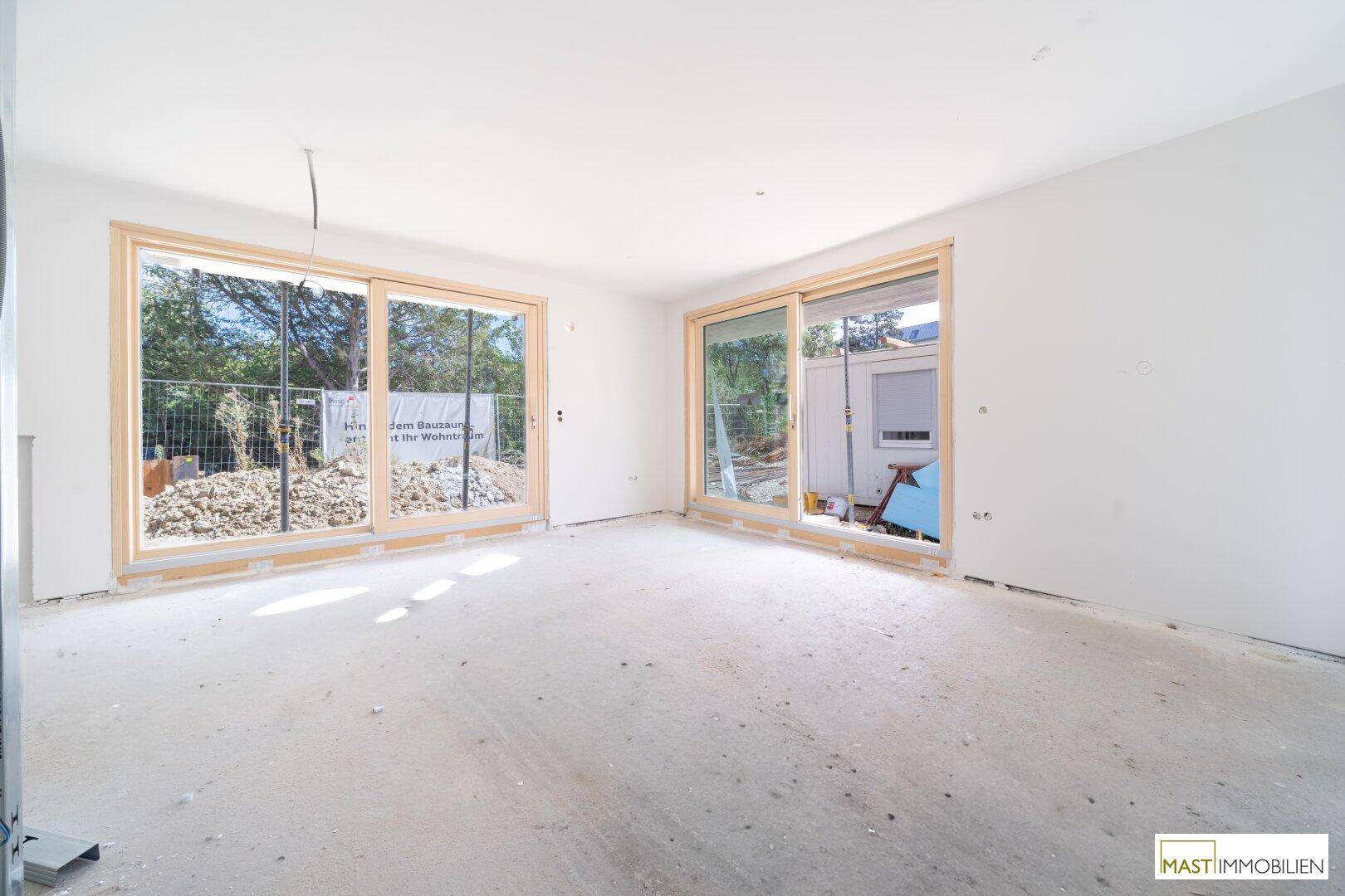 Heller, unfertiger Wohnraum mit großen Schiebetüren und Blick auf die Baustelle im Außenbereich.