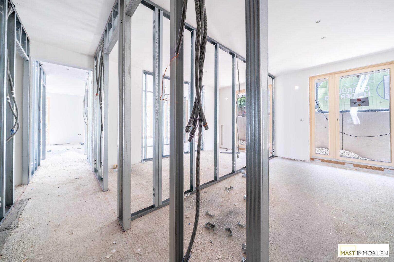 Innenraum im Rohbau mit sichtbaren Metallständerwänden, Verkabelung und Fenstern im Hintergrund.