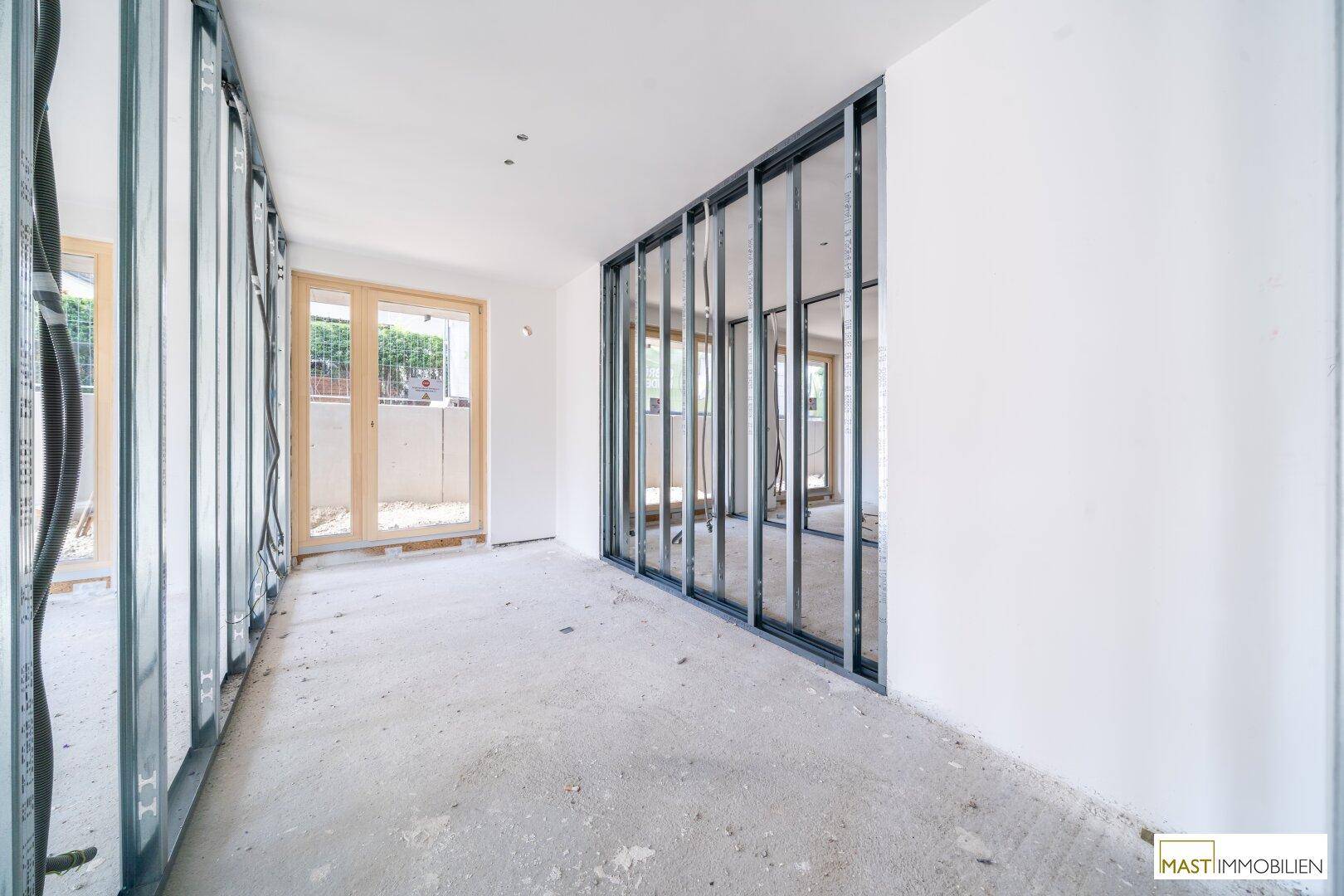 Rohbau eines langen Raumes mit Betonboden, weißen Wänden und Metallständerwerk für die Innenwände.