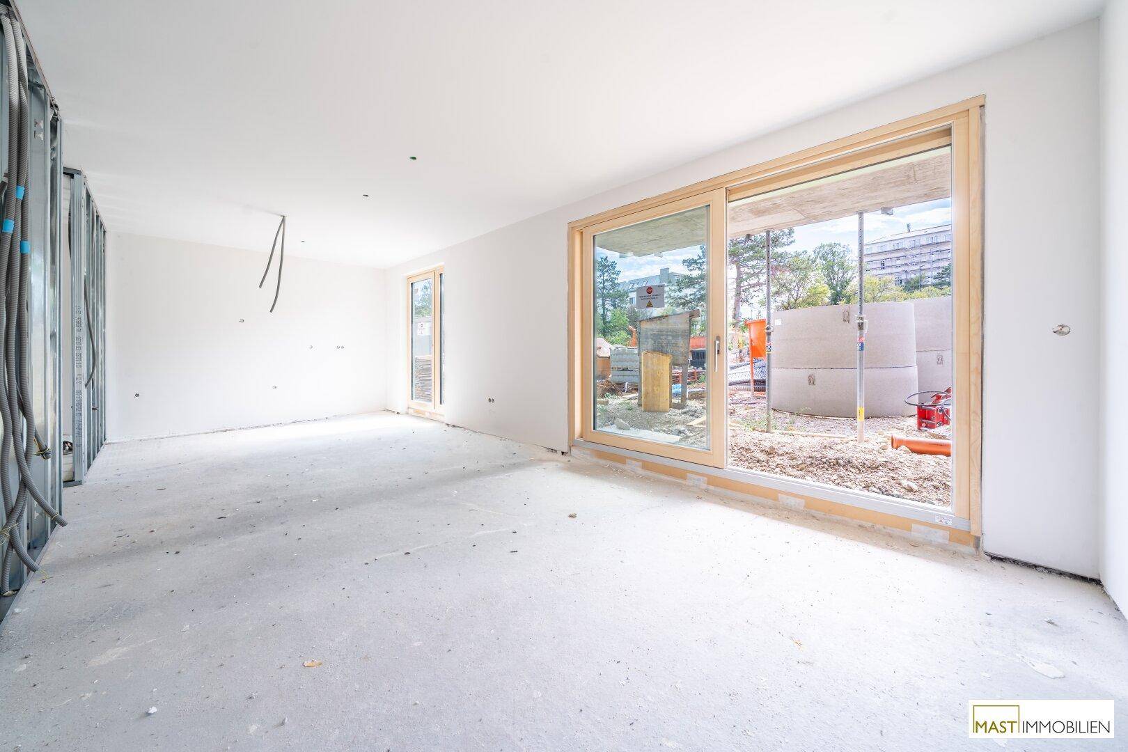 Unfertiger Innenraum mit großen Schiebetüren und Blick auf die Baustelle, bereit für den Ausbau.