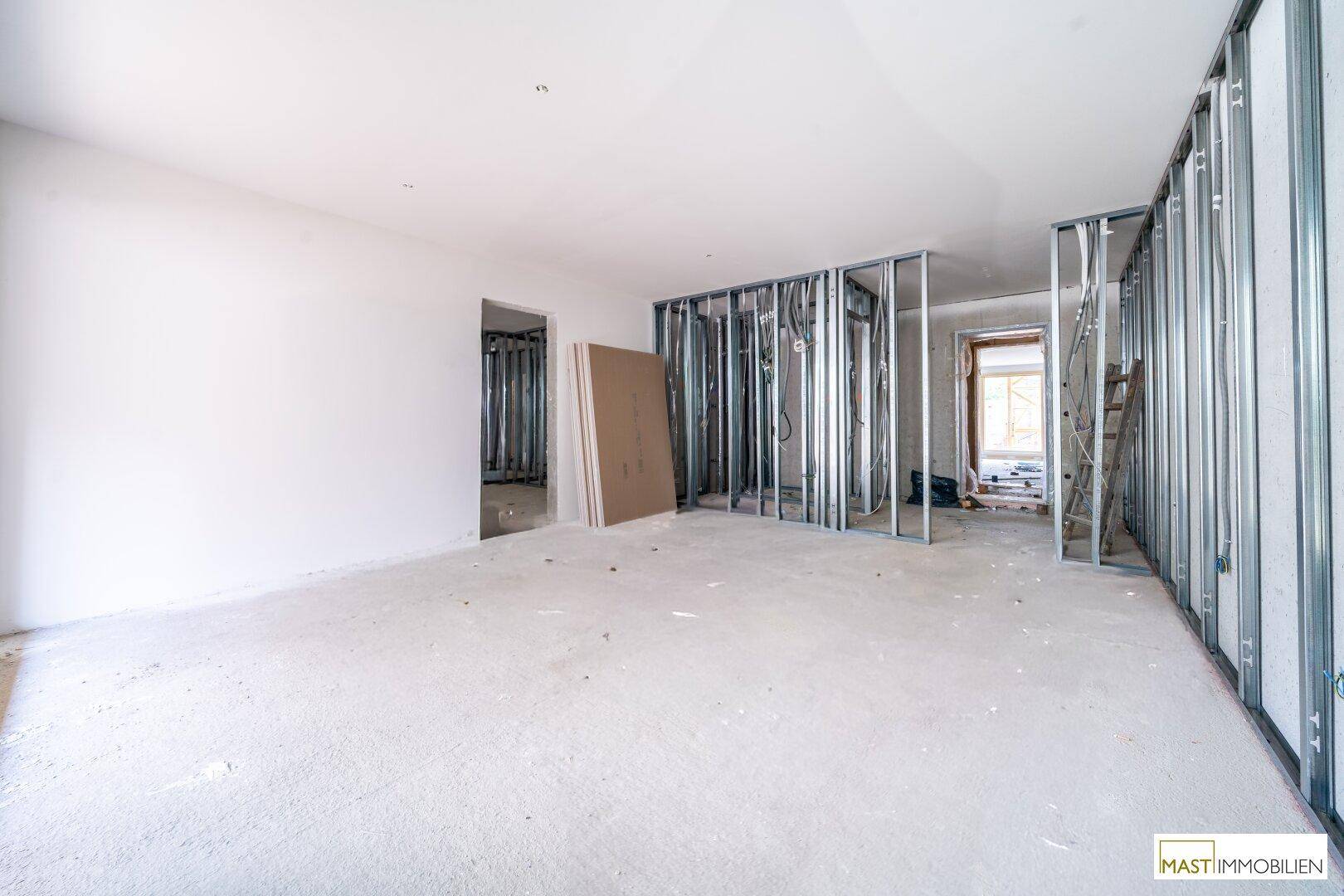 Geräumiger Rohbau-Raum mit sichtbaren Metallständerwänden und vorbereiteten Installationen.