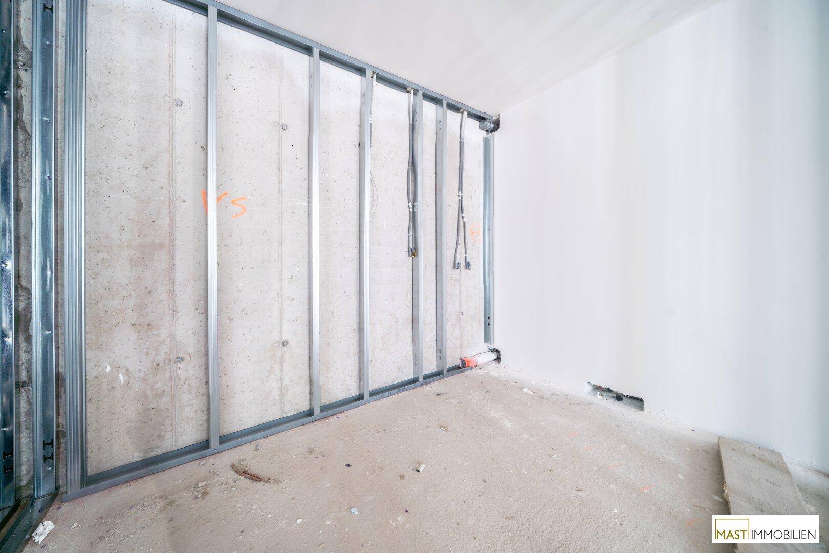 Detailansicht einer Wand im Rohbau mit Metallständerwerk und sichtbarer Verkabelung.