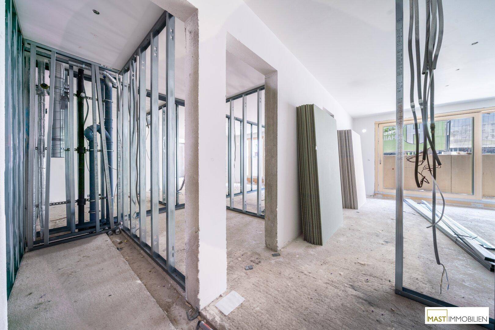 Innenraum im Rohbau mit Metallständerwerk und Baumaterialien.