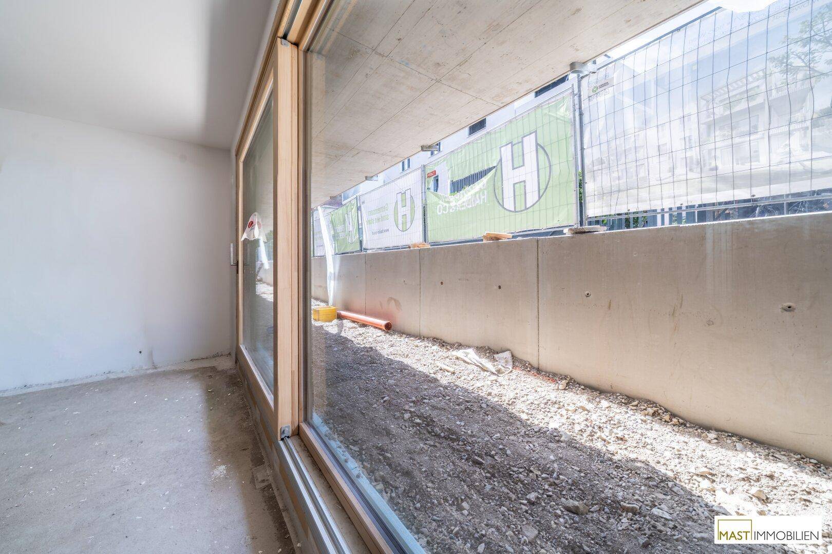 Unfertiger Innenraum mit großen Fenstern und Blick auf die Baustelle.