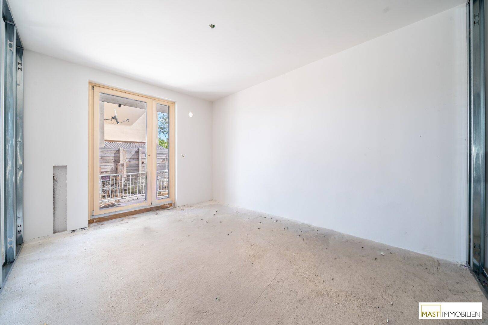 Rohbau-Zimmer mit Zugang zu einem kleinen Außenbereich und viel Tageslicht.