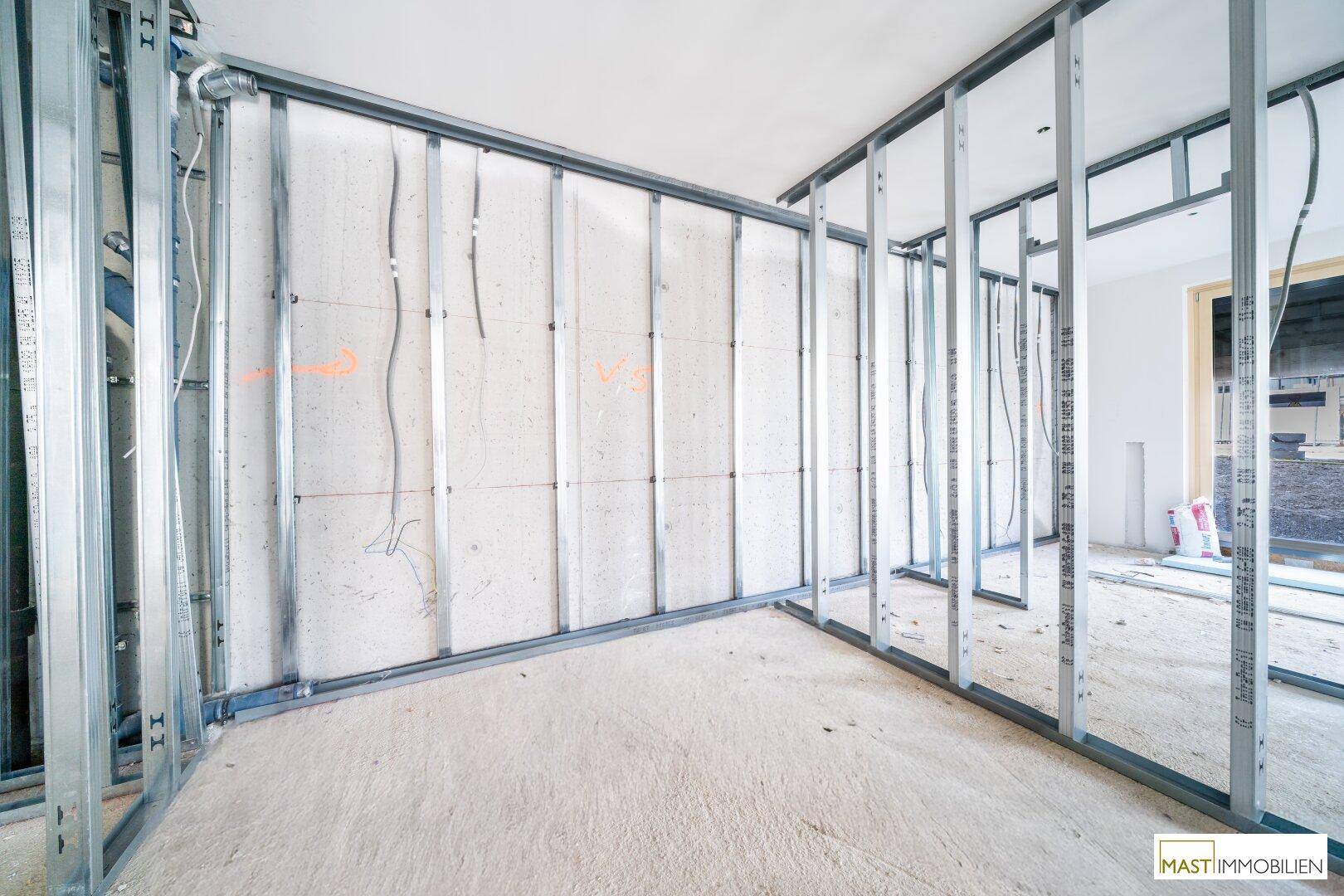 Rohbau-Innenansicht mit Metallständerwerk und sichtbaren Elektroinstallationen.
