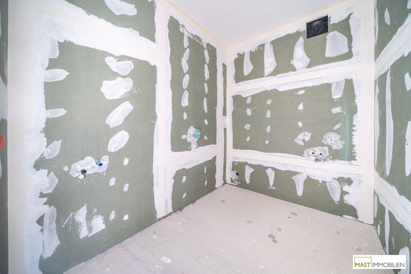 Badezimmer im Rohbau mit vorbereiteten Anschlüssen für Waschbecken und Dusche oder Badewanne.