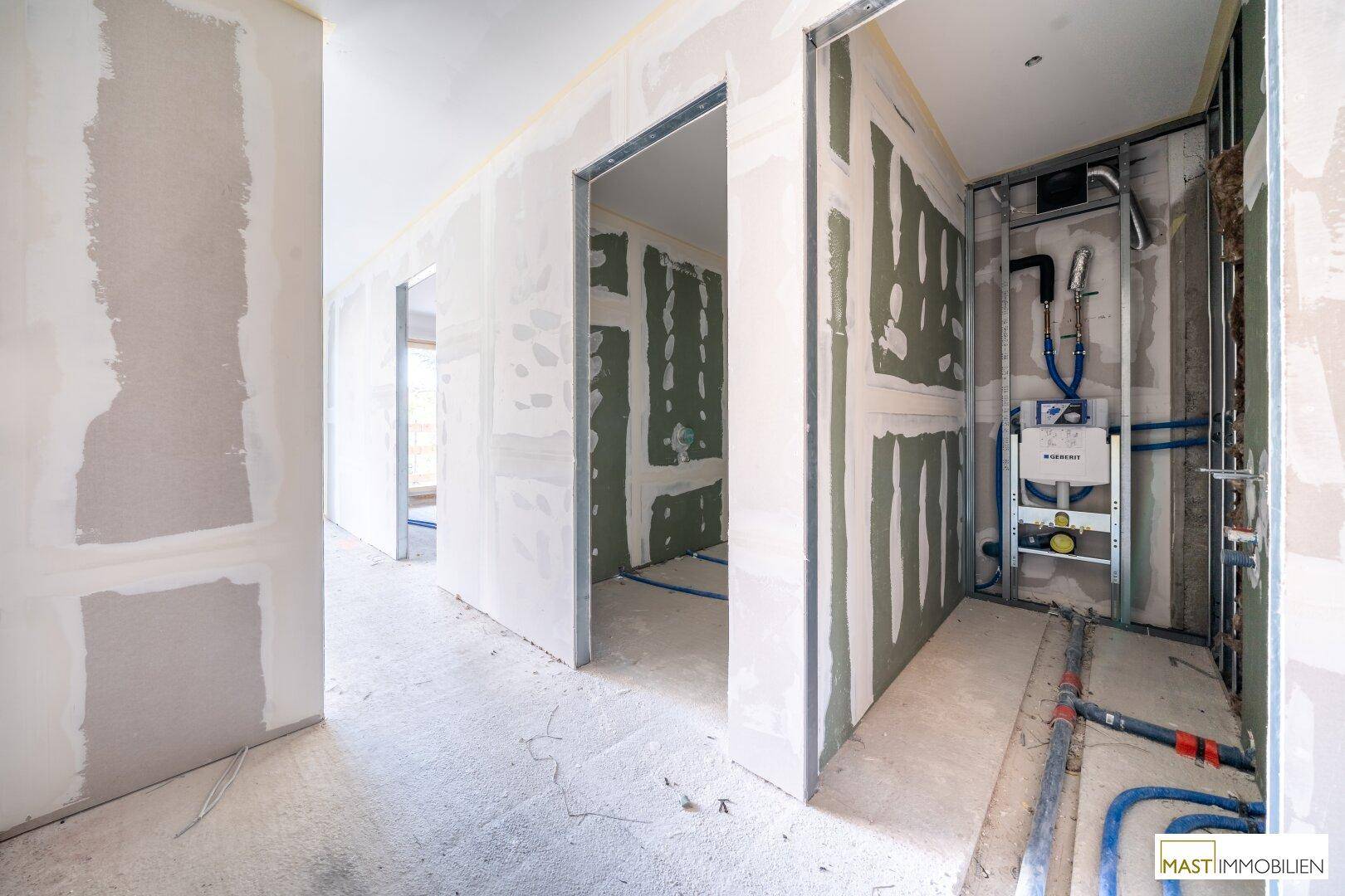 Flur im Rohbau mit Trockenbauwänden und vorbereiteten Sanitärinstallationen für ein Badezimmer oder WC.
