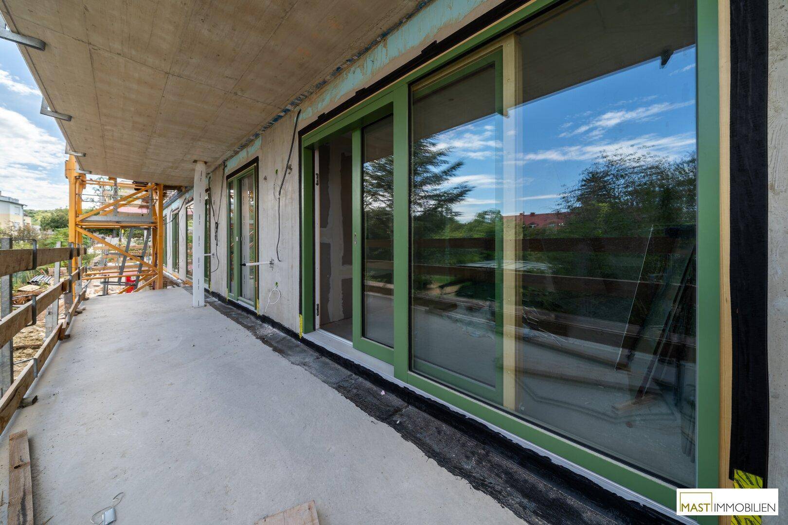 Breiter Balkon im Rohbau mit großen grünen Schiebetüren und Blick auf die Baustelle.