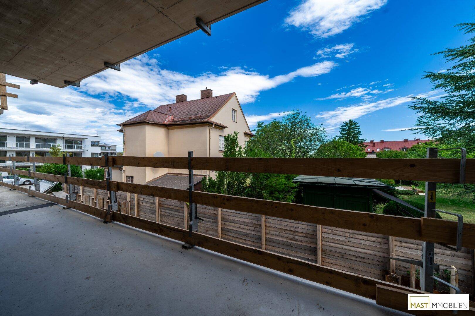 Balkon im Rohbau mit Holzsicherung und Blick auf die umliegenden Häuser und viel Grün.