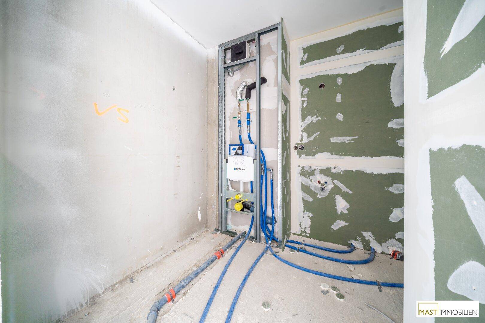 Rohbau eines Badezimmers mit vorinstallierten Sanitärleitungen und feuchtigkeitsbeständigen Wänden.